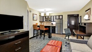 A compact hotel room with a kitchenette, a flat-screen TV, a sofa, a dining table, and a small red bench. - Staybridge Suites Mt. Juliet - Nashville Area by IHG (Mount Juliet)