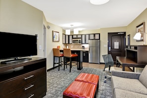 A compact hotel room with a kitchenette, a flat-screen TV, a sofa, a dining table, and a small red bench. - Staybridge Suites Mt. Juliet - Nashville Area by IHG (Mount Juliet)