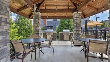 Un patio exterior con pilares de piedra, una parrilla y mesas con sillas.