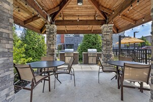 An outdoor patio with stone pillars, a grill, and tables and chairs.
