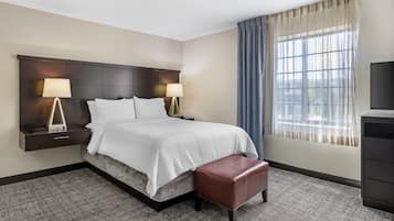 A hotel room with a bed, bedside tables, lamps, a TV, a window with curtains, and a carpeted floor.