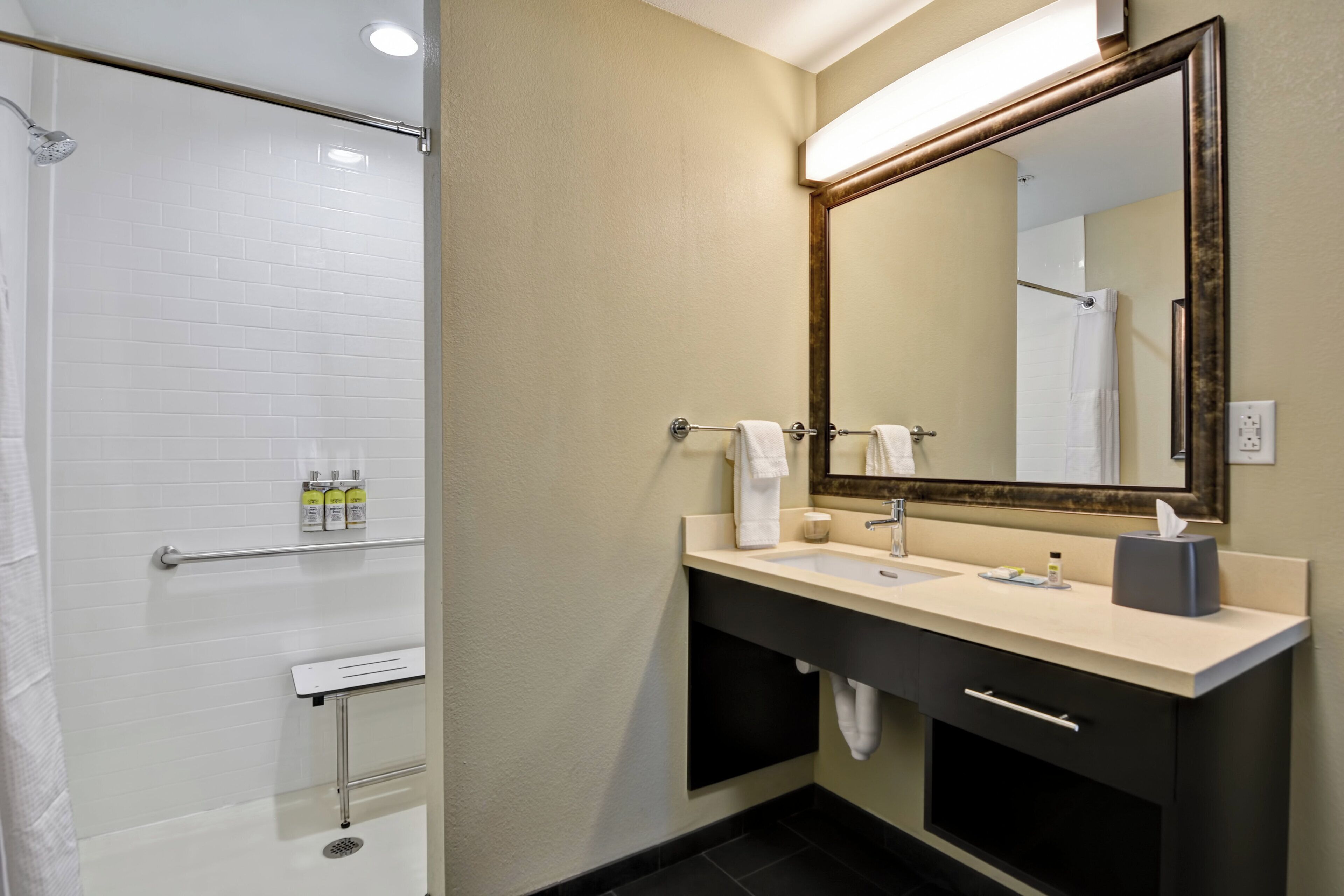 A bathroom with a shower, a sink, a mirror, and toiletries.