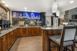 A modern kitchen with a cityscape mural, a coffee station, and a stone fireplace. - Staybridge Suites Mt. Juliet - Nashville Area by IHG (Mount Juliet)