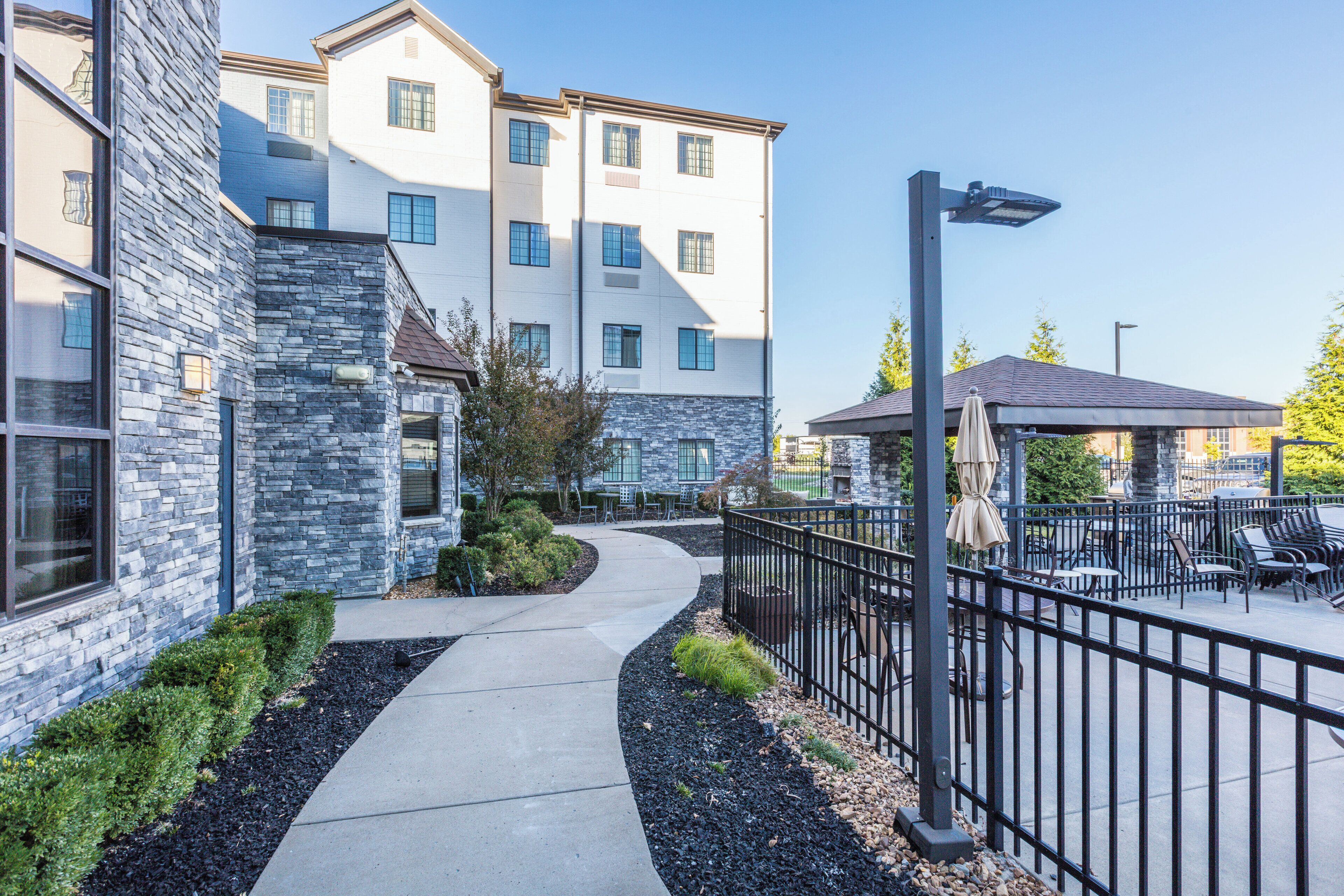 A modern building with a stone facade, a curved pathway, outdoor seating, and a covered area.