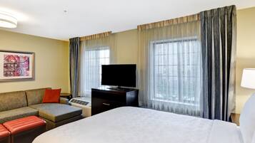 A hotel room with a bed, a sofa, a TV, and a window with curtains.