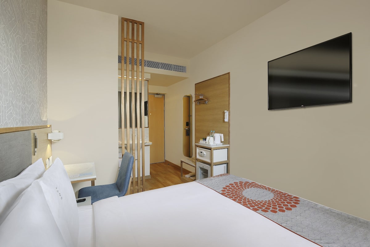 A hotel room with a bed, a desk, a chair, a TV, a mirror, and a wardrobe.