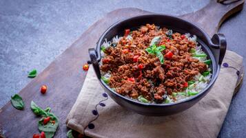 A bowl of rice and meat dish on a wooden board.