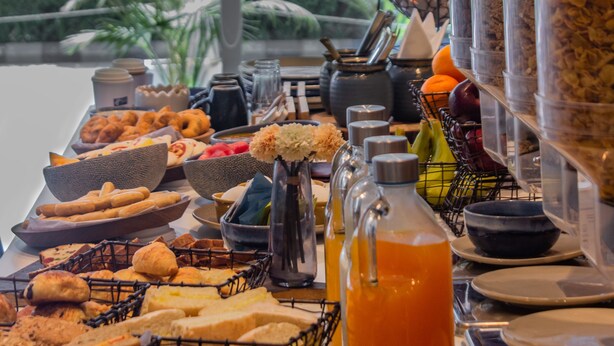 Un bufé con diversos alimentos, incluyendo pan, pasteles y frutas, con vistas al exterior con vegetación.
