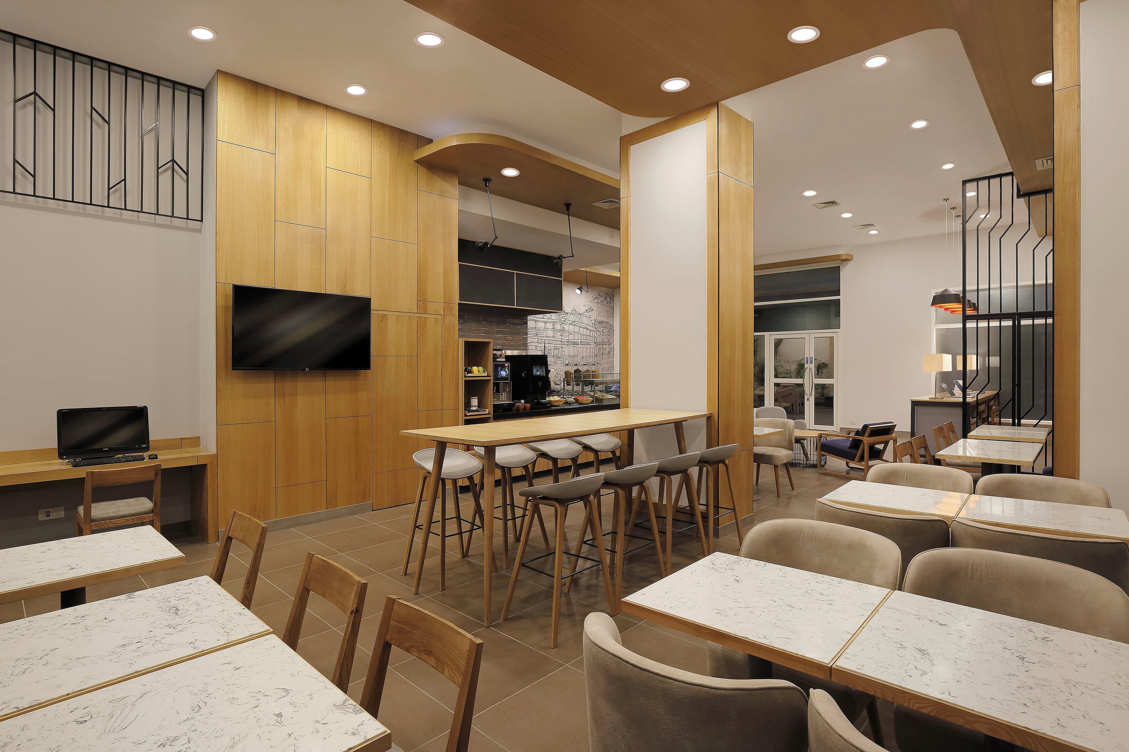 A modern dining area with bar stools, tables, and a flat-screen TV mounted on the wall.
