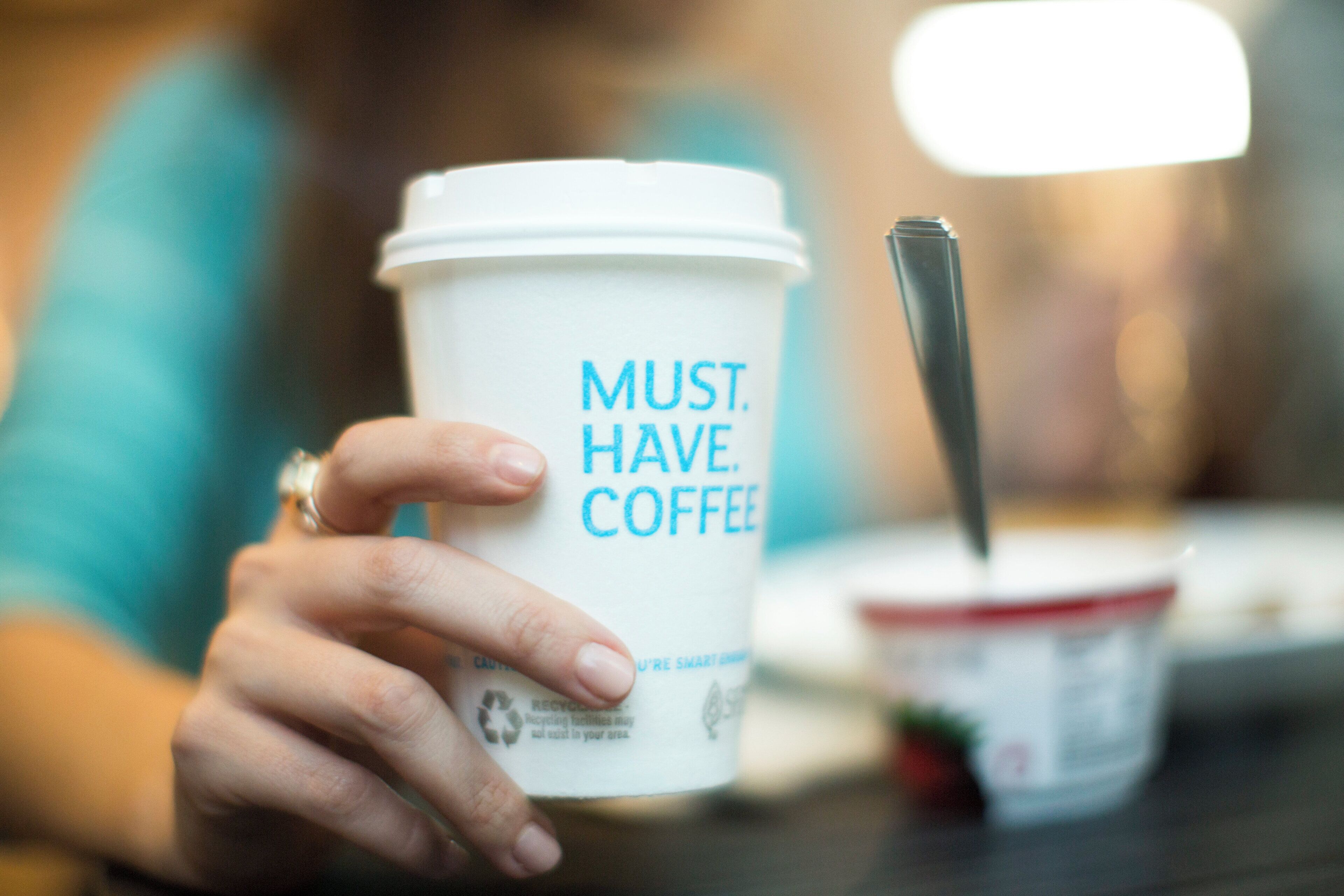 A hand holding a coffee cup with the text 'MUST HAVE COFFEE' on it.
