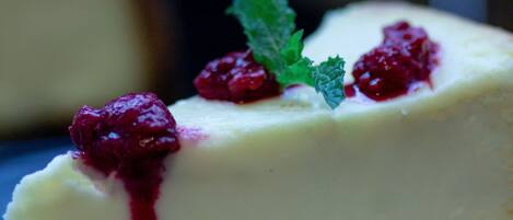 Une part de gâteau au fromage, accompagnée d’une compote de fruits rouges et décorée de quelques feuilles de menthe, présentée sur une assiette.