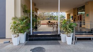 Entrada de un hotel con un área de estar al aire libre techada, plantas en macetas y una escalera que lleva a la entrada.