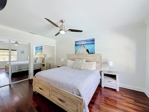Una camera da letto con un letto, un comodino, uno specchio, una ventola a soffitto e un quadro appeso al muro.