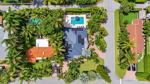 An aerial view of a residential area with a swimming pool, a house with a red roof, and surrounding greenery.