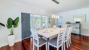 A dining area with a white table and chairs, a potted plant, and a view through glass doors.