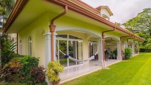 A house with a covered porch, a hammock, and a well-maintained lawn. - Los Suenos Resort Colina 8E (Jacó)