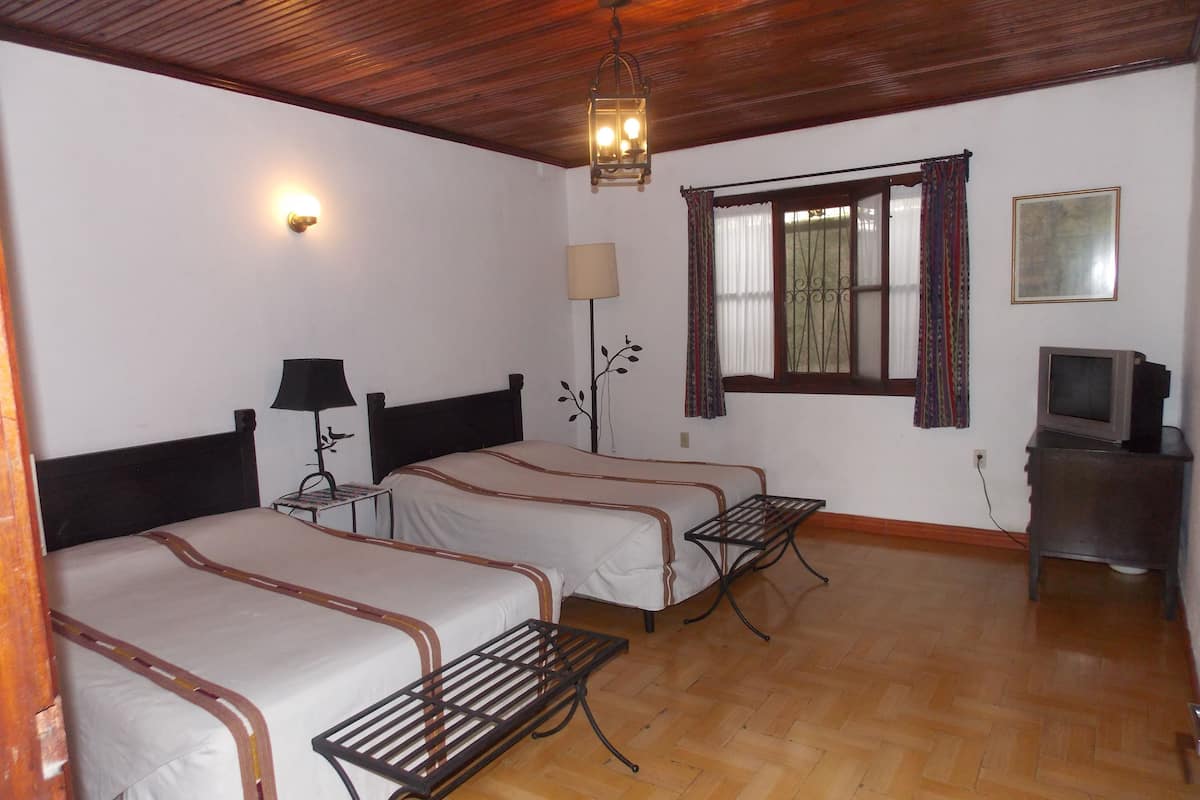 A room with two beds, a desk, a lamp, a television, and a window with curtains.
