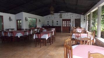 Un comedor amplio con varias mesas y sillas, techo alto y vistas a zonas verdes.