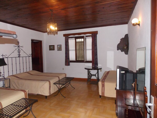 A room with two beds, a small table, a chair, a television, and a window with curtains. - Hotel Casa Duranta (Cobán)
