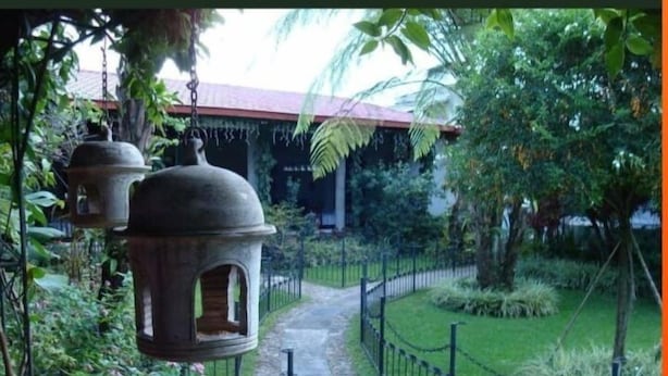 Un sendero conduce a un edificio de techo rojo, rodeado de follaje y una cerca de alambre.