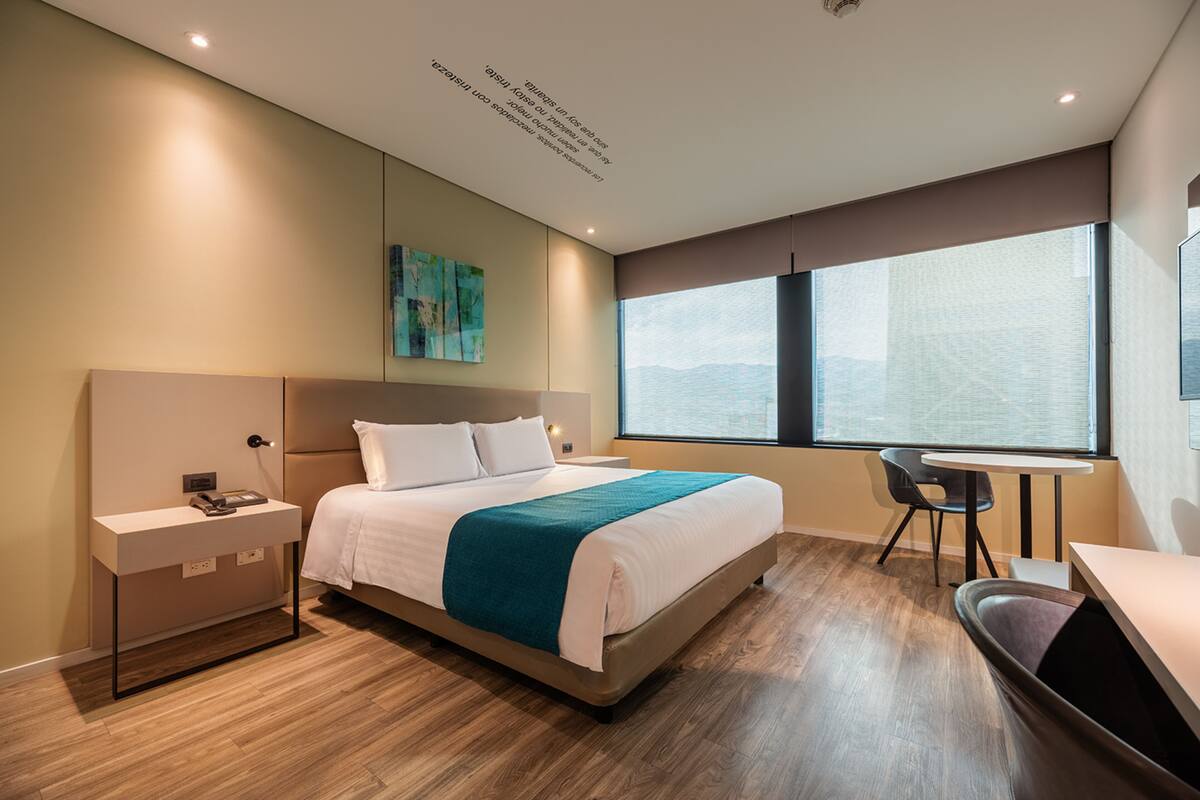 Una habitación de hotel moderna con una cama grande, mesita de noche y un escritorio con silla.
