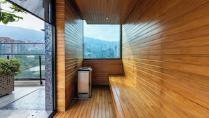 A narrow corridor with wooden walls and a bench, leading to a window with a cityscape view. - Estelar Square (Medellín)