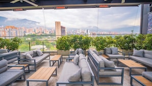An outdoor seating area with sofas and tables, a city view, and potted plants. - Estelar Square (Medellín)