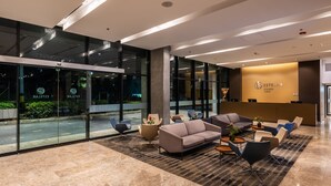 A modern hotel lobby with a reception desk, seating area, and large glass windows. - Estelar Square (Medellín)