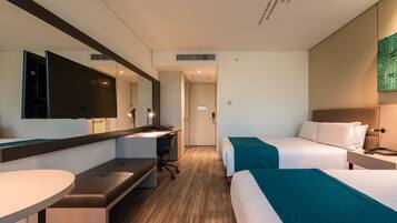 A hotel room with a desk, two beds, a mirror, and a wall-mounted artwork.