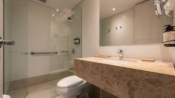 A modern bathroom with a glass shower enclosure, a beige marble countertop, and a large mirror above the sink.