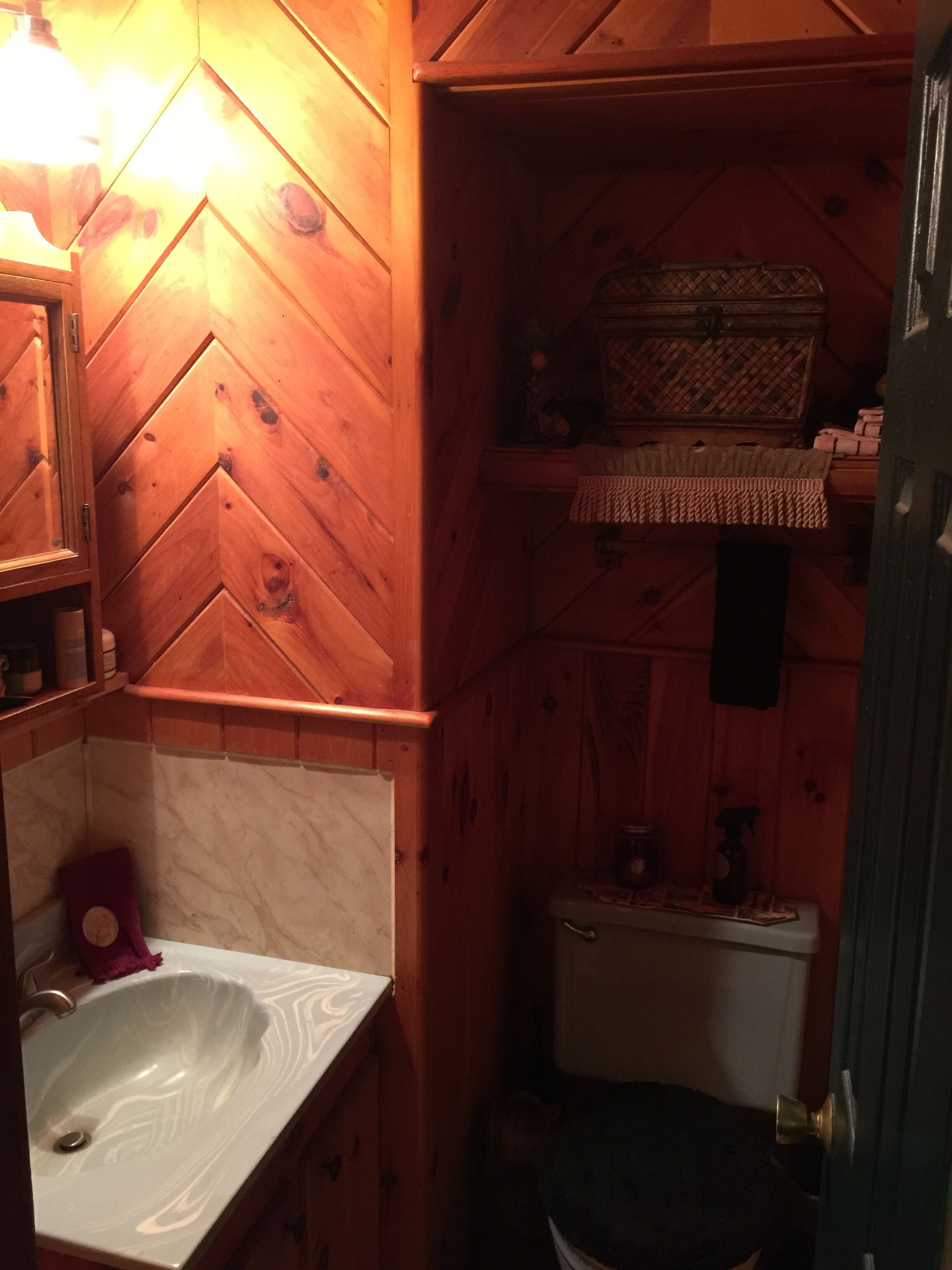 Et badeværelse i træ med en hvid vask, toilet og spejl.