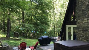 Un espace extérieur rustique avec un bâtiment en pierre, un jacuzzi et des fauteuils Adirondack rouges.