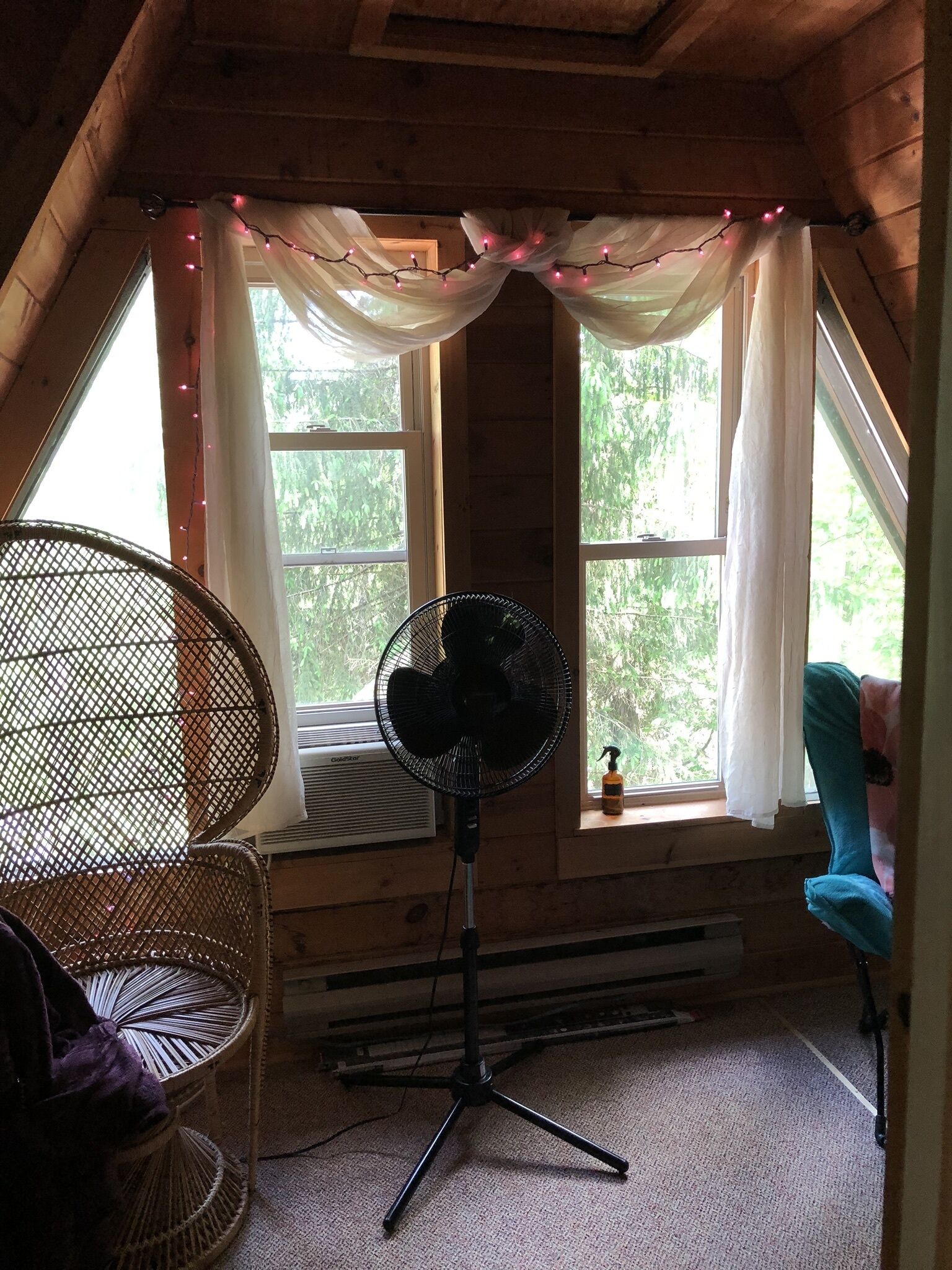 A cozy room with a fan, wicker chair, and a window with curtains.
