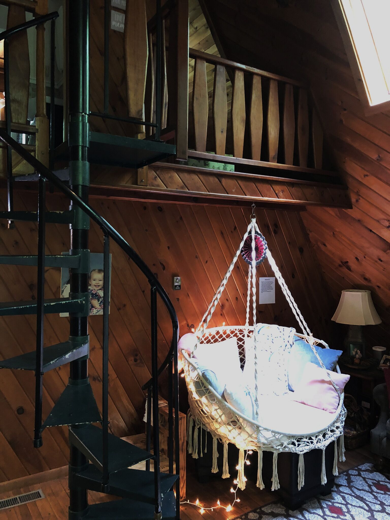 Un intérieur en bois avec un escalier en colimaçon, une chaise suspendue et une lampe.