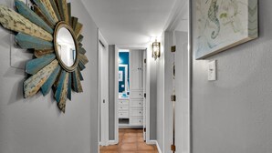 A hallway with a decorative mirror, a light fixture, and a door leading to a bathroom. - Beachfront Condo directly on the Beach -1st Floor; Newly Remodeled (South Padre Island)
