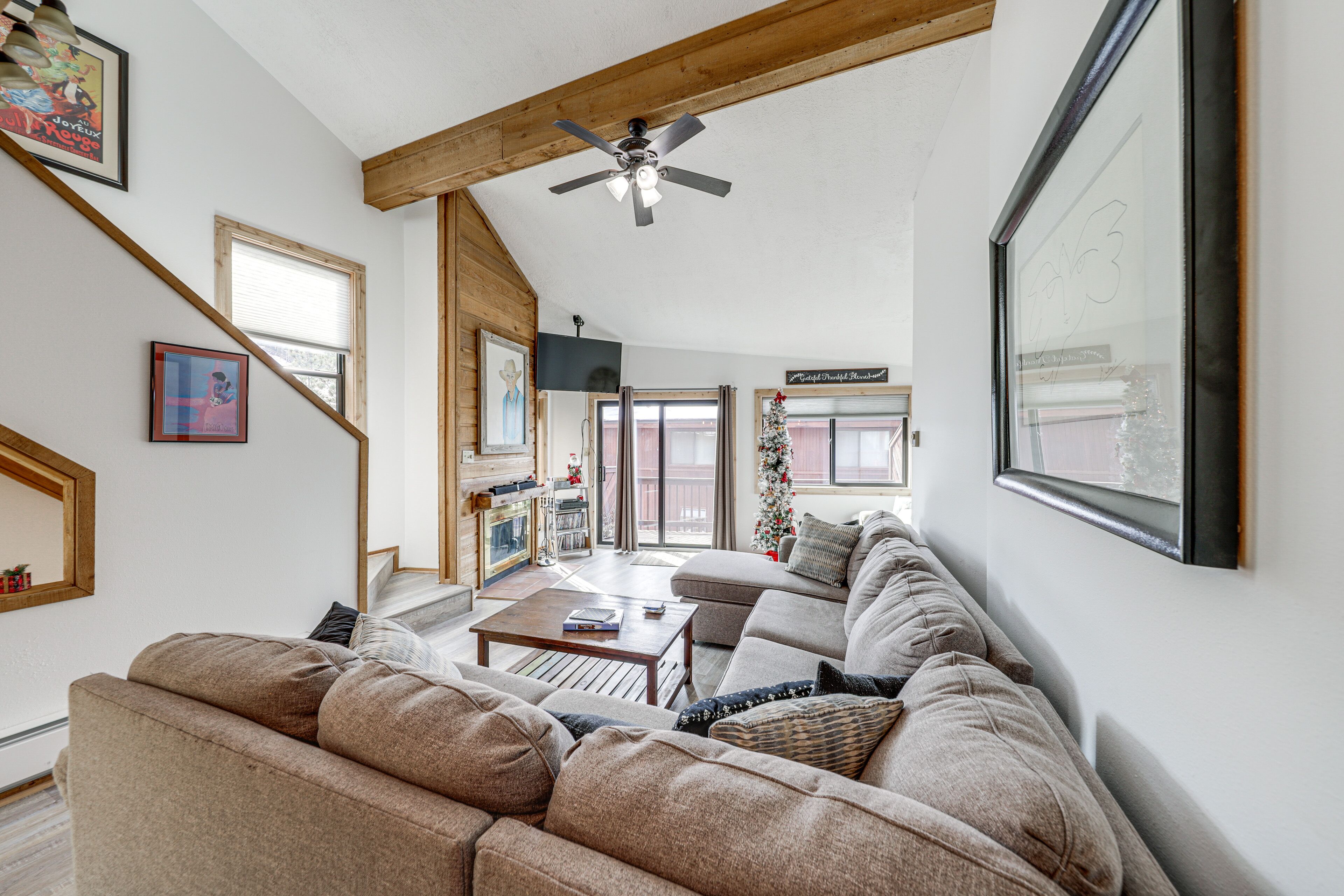 Ein großzügiges Wohnzimmer mit einer großen Eckcouch, einem Deckenventilator aus Holz und Blick auf einen Balkon.