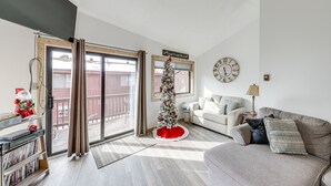 A living room with a Christmas tree, a sofa, a coffee table, a bookshelf, and a sliding glass door leading to a balcony. - Angel Fire Resort Condo, 400 Feet to Chile Express (Angel Fire)