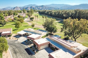 A golf course with residential buildings, a parking area, and a mountainous backdrop.