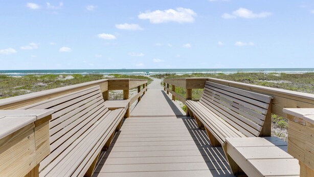 Ein Holzsteg führt zum Strand, entlang befinden sich Bänke auf beiden Seiten.