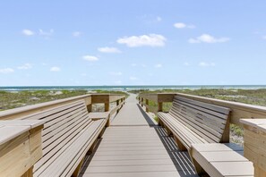 A wooden boardwalk leading to the beach with benches on either side.