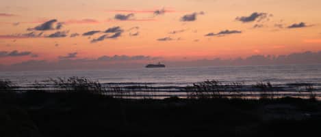 Een zonsondergang boven de zee, met een schip in de verte.