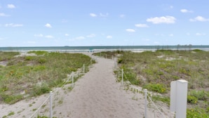 Ein sandiger Küstenpfad führt zum Meer, mit einer Umzäunung und einem Wegweiser.