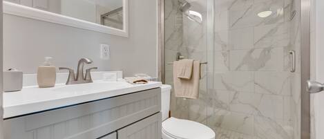 Un baño con ducha envuelta en vidrio, inodoro blanco y tocador con espejo y dispensador de jabón.