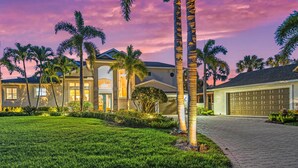 A two-story house with a well-maintained lawn, palm trees, and a garage. - The Sun Dial | Waterfront Home on Siesta Key w/ Private Pool & Large Backyard, Close to Beach! (Siesta Key)