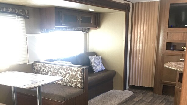 A compact RV interior with a sofa, a small table, and a television mounted on the wall. - Best price, clean and new rv  trailer  (Los Angeles)