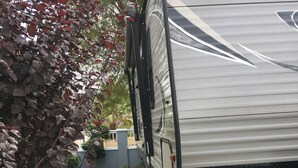 A stationary RV with a visible brand name, a concrete driveway, and surrounding vegetation. - Best price, clean and new rv  trailer  (Los Angeles)