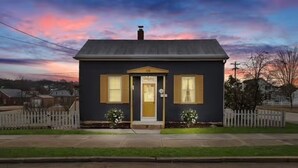 A two-story house with a dark facade, a central entrance, and a picket fence in the front yard. - Private Guest House-Hermann MO (Hermann)