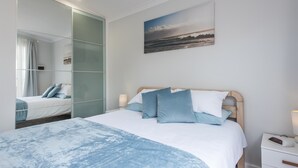 A bedroom with a bed, a bedside table, a nightstand, a mirror, and a painting on the wall. - Prestigious Northshore Guest House - Comfortable Living Close To Mullaloo Beach (Kallaroo)