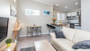 A modern living room with a beige sofa, a TV, and a dining area with a table and chairs. - Prestigious Northshore Guest House - Comfortable Living Close To Mullaloo Beach (Kallaroo)