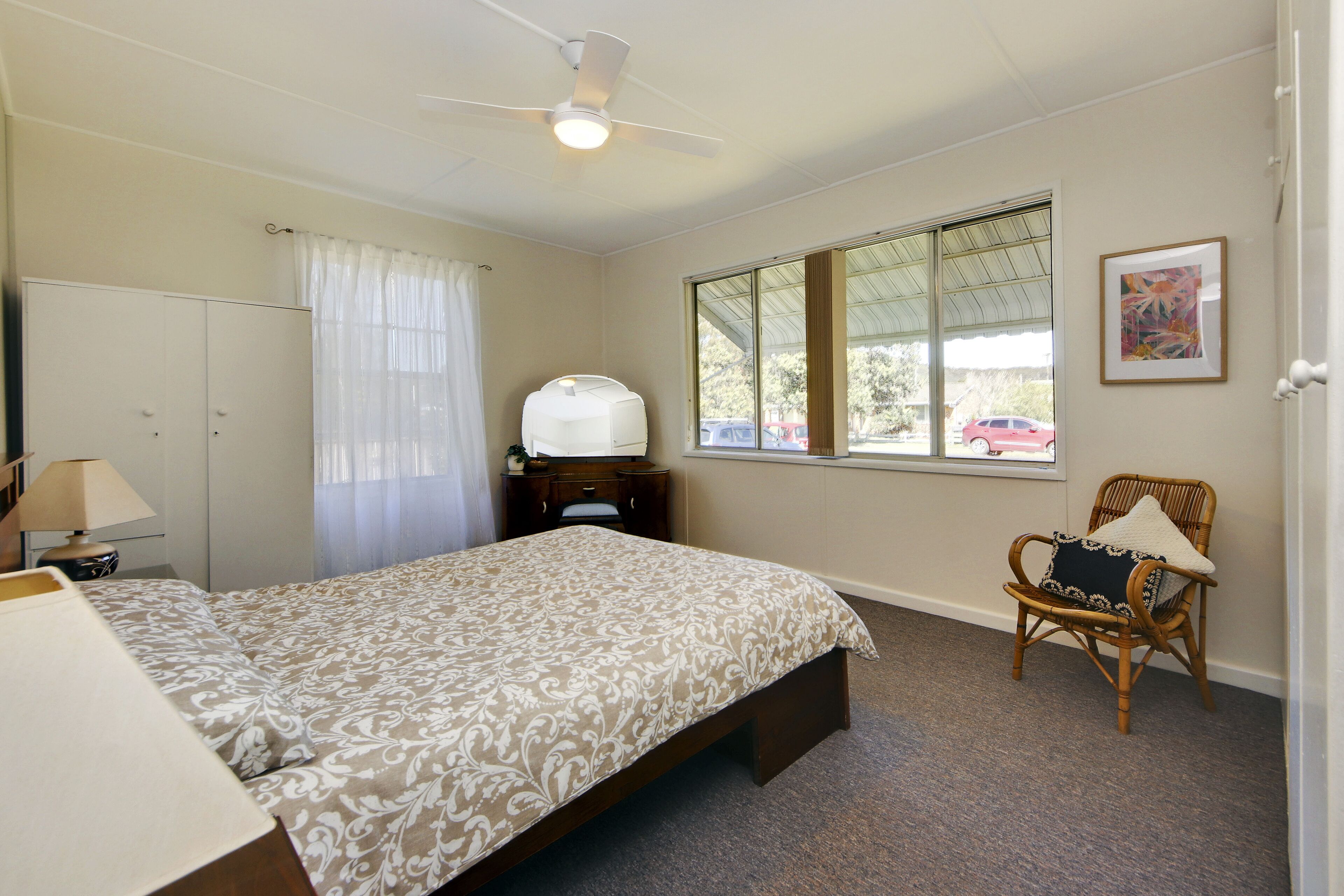 A bedroom with a bed, a chair, a wardrobe, a window, and a ceiling fan.